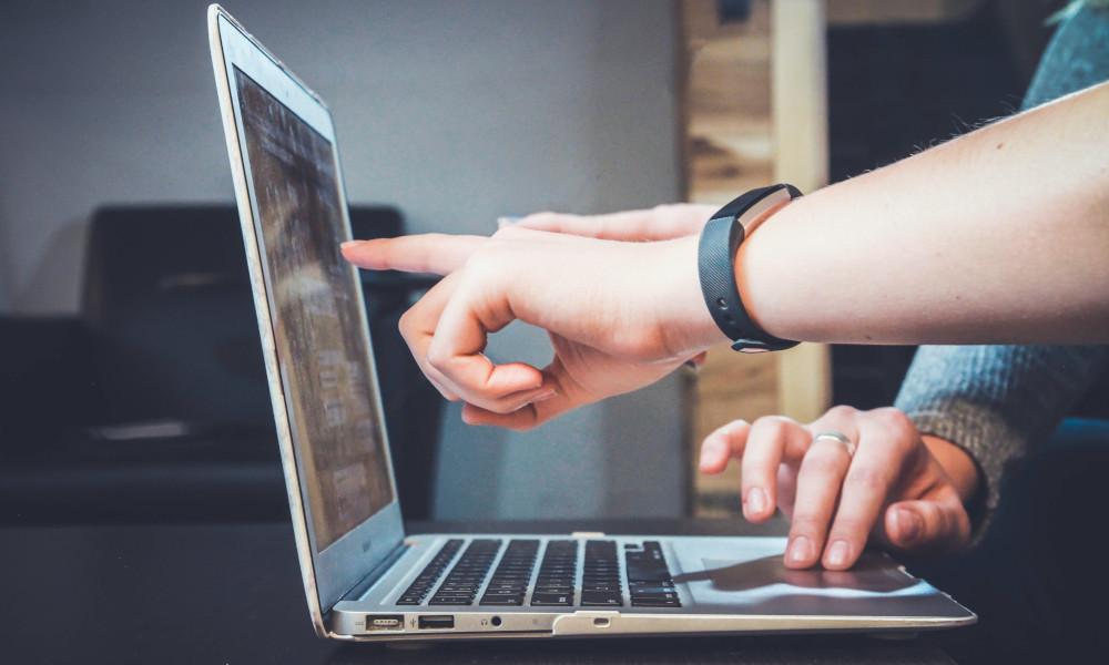 Hands pointing at a laptop screen while another person uses the mouse