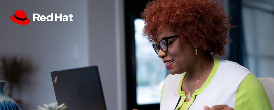 Image of a woman using her computer with the Red Hat logo added in the upper left where it is on a clear background.