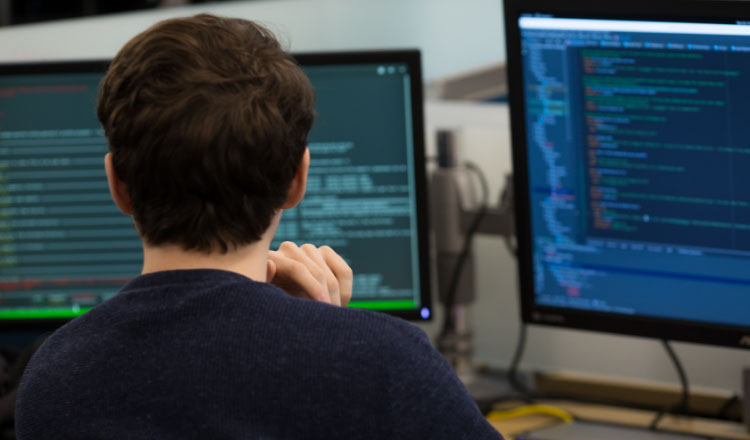 Ein IT-Fachmann arbeitet an einem Schreibtisch mit mehreren Computermonitoren, auf denen Code angezeigt wird.