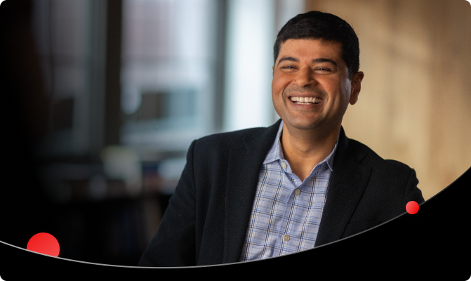 A man in a blazer and plaid shirt laughs heartily in an office setting