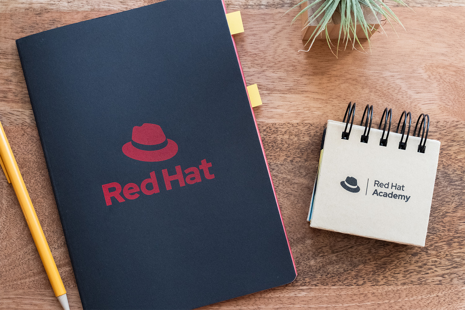 A black notebook with the stacked Red Hat logo in red, and a flip book of bookmark stickies with the Red Hat Academy logo in black.