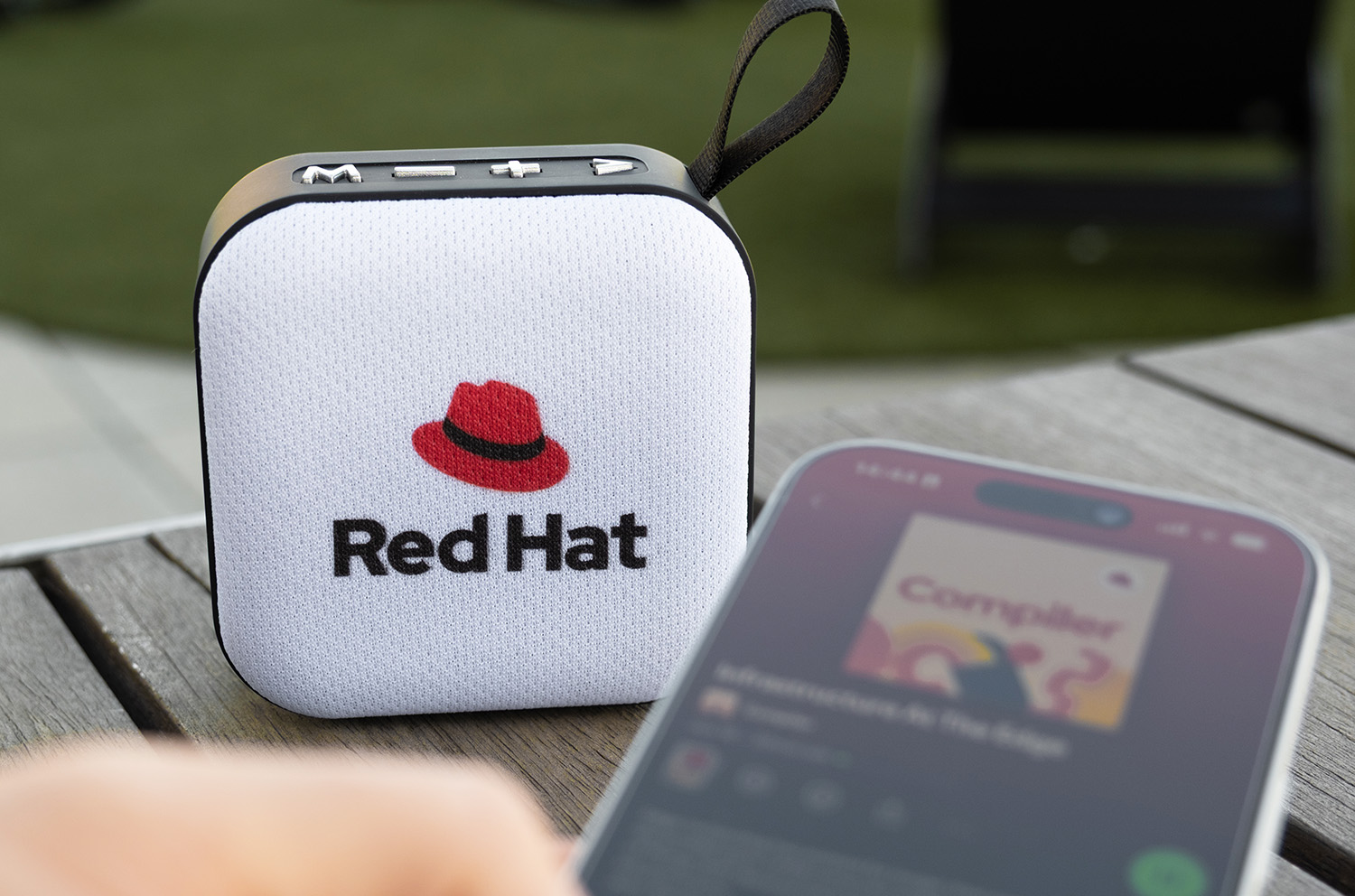 A small bluetooth speaker with the stacked Red Hat logo printed on the front fabric mesh.