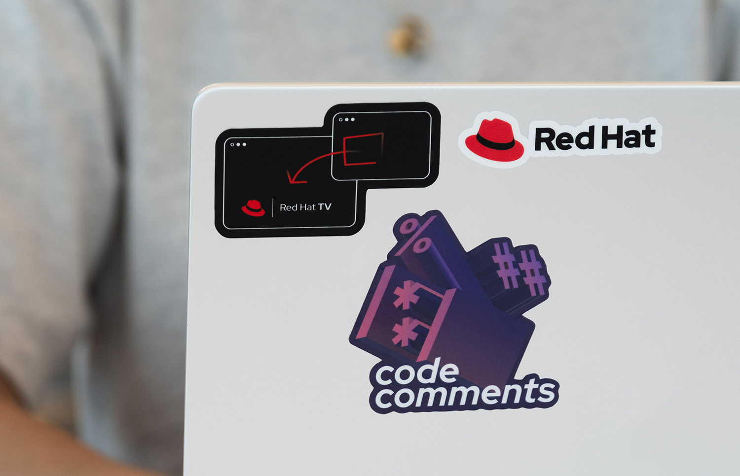 A laptop with custom stickers for the Code Comments podcast and Red Hat TV.