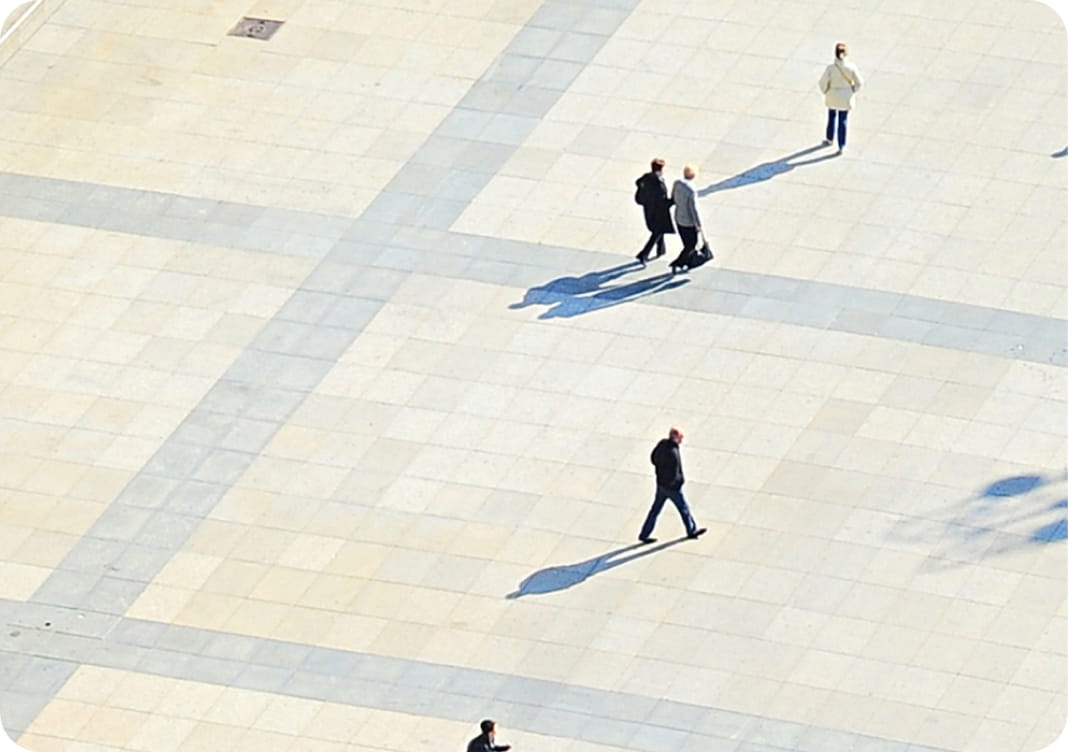 High-angle view of people crossing a large plaza and casting long shadows