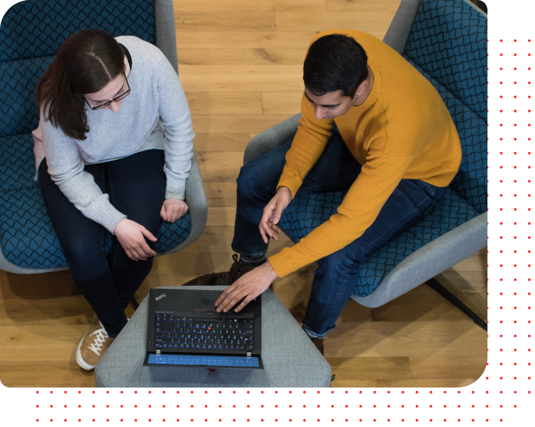 Overhead view of two colleagues in blue chairs collaborating on a laptop in a modern office space