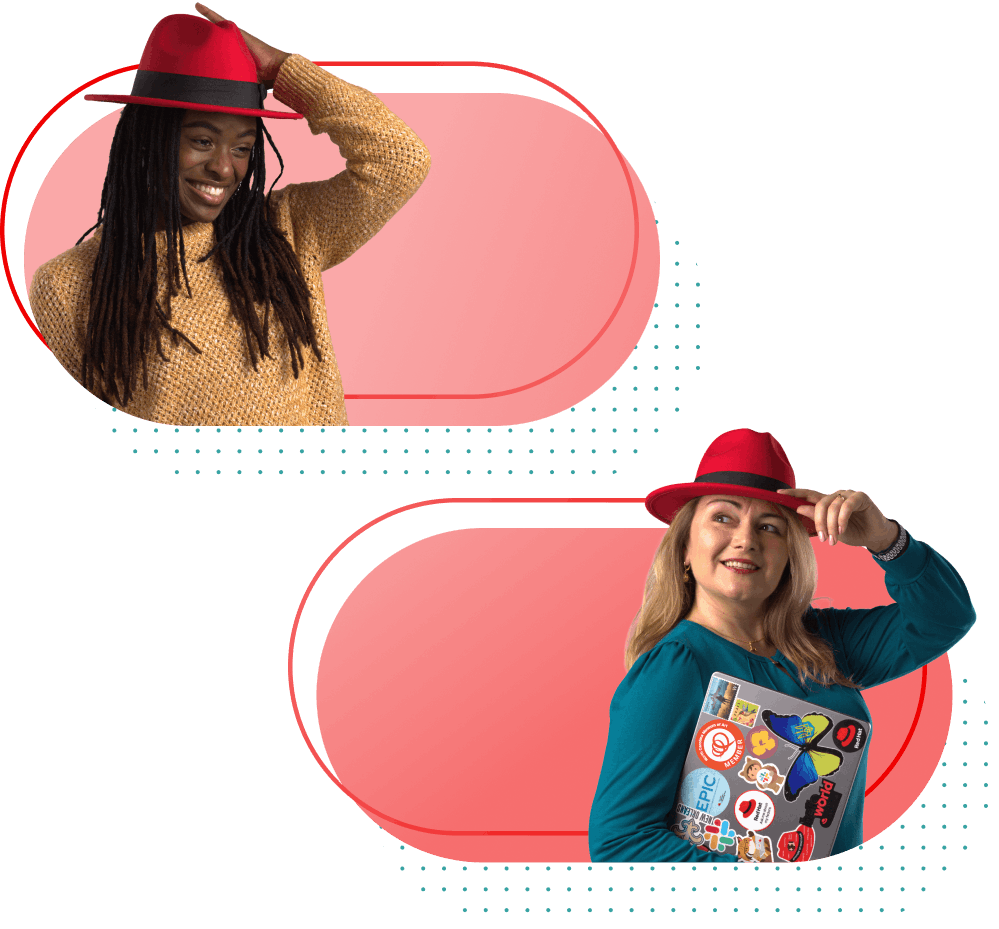 Two smiling women tip their red fedoras, one holding a laptop covered in stickers
