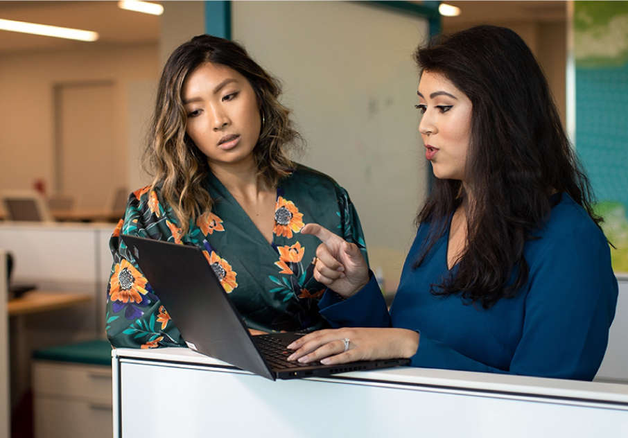 Two women discuss work on a laptop in an office as one points to the screen