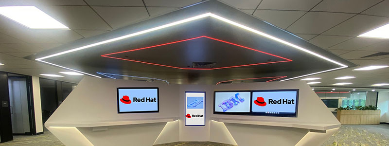 A modern Red Hat reception area with a geometric desk, multiple screens, and overhead lighting