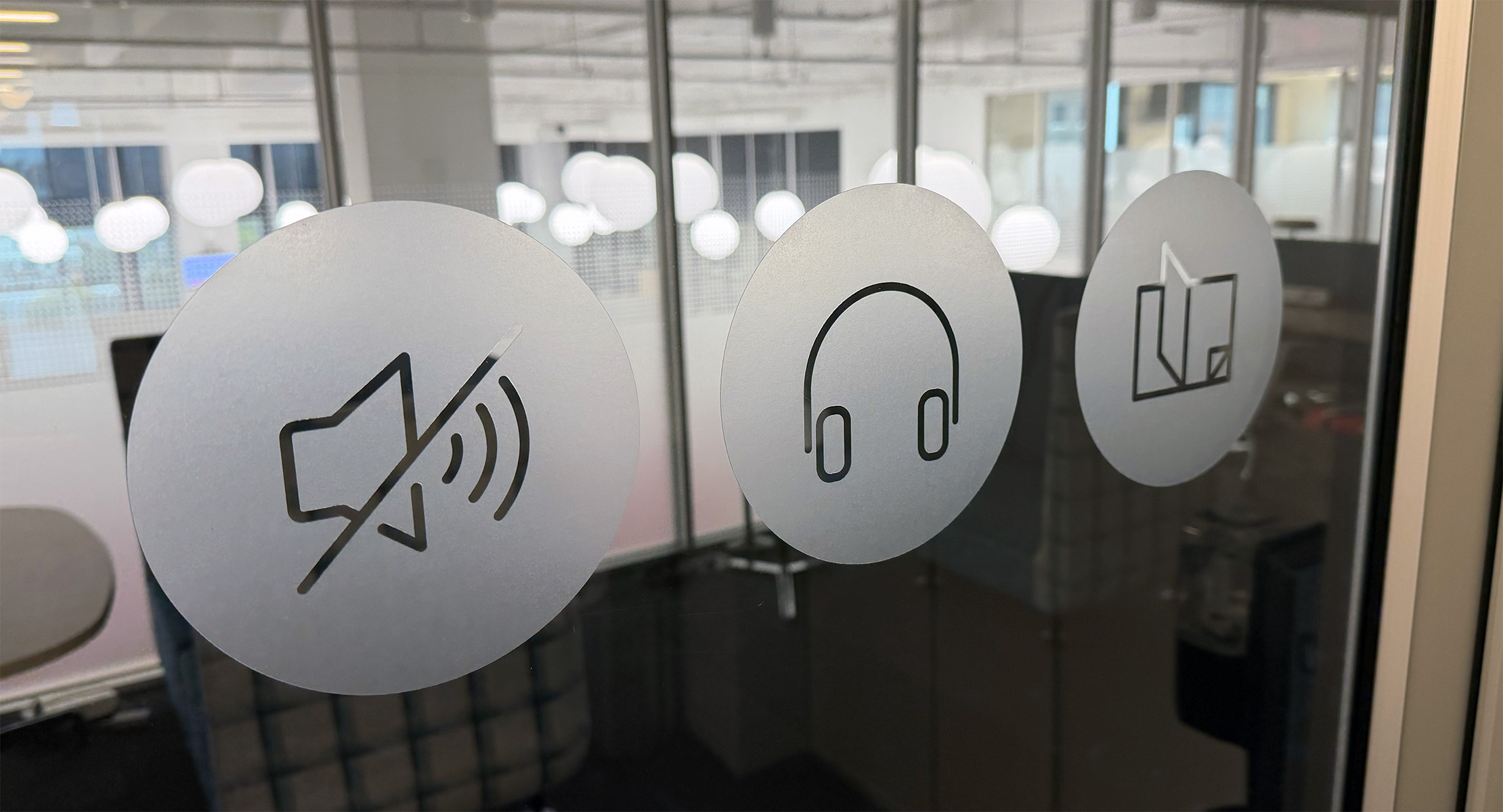 A photo shows the glass door to the library at Red Hat tower featuring 3 circles of window cling. Each circle has a Red Hat icon in the center, representing 