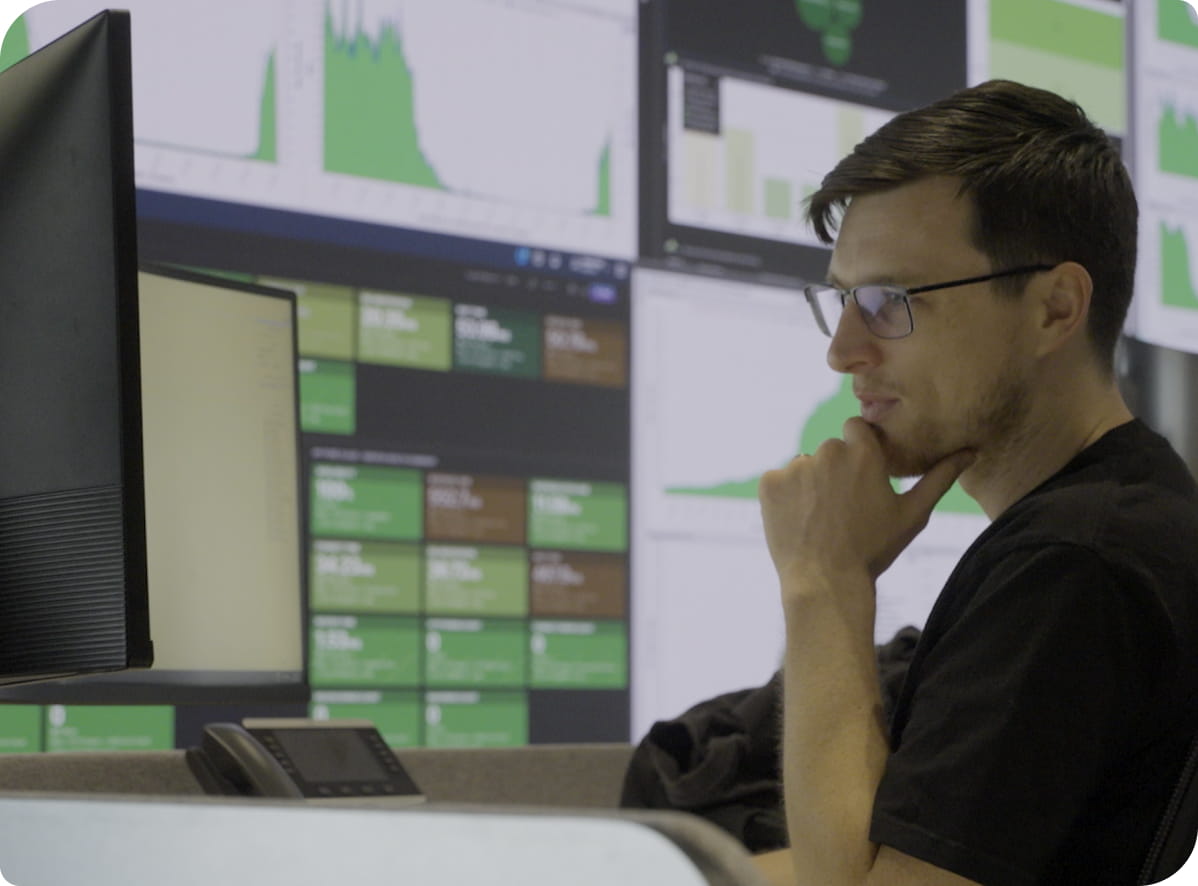 An IT professional thoughtfully studies charts and graphs across multiple computer screens