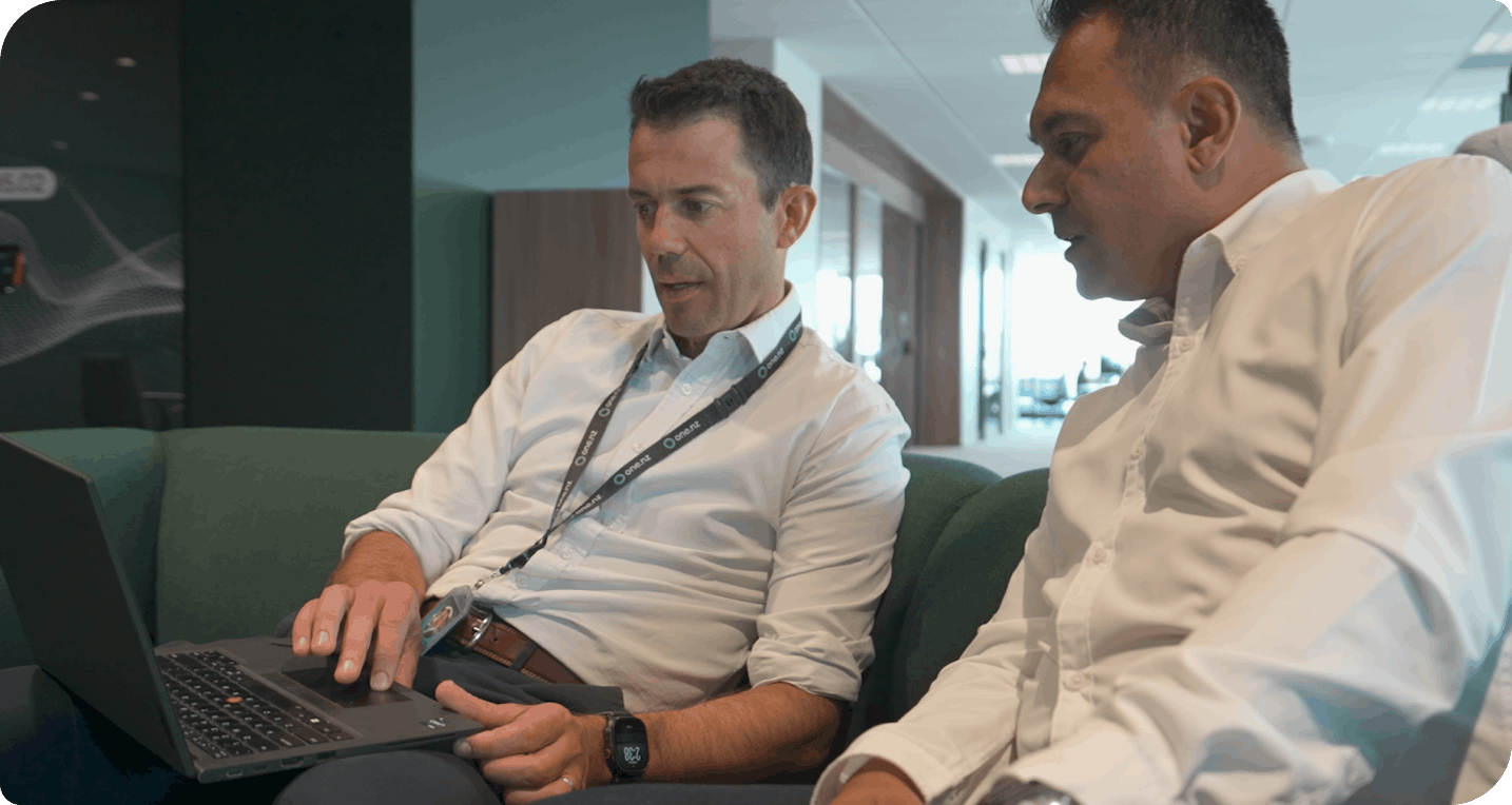 Two employees in an office collaborating over a laptop on a green couch
