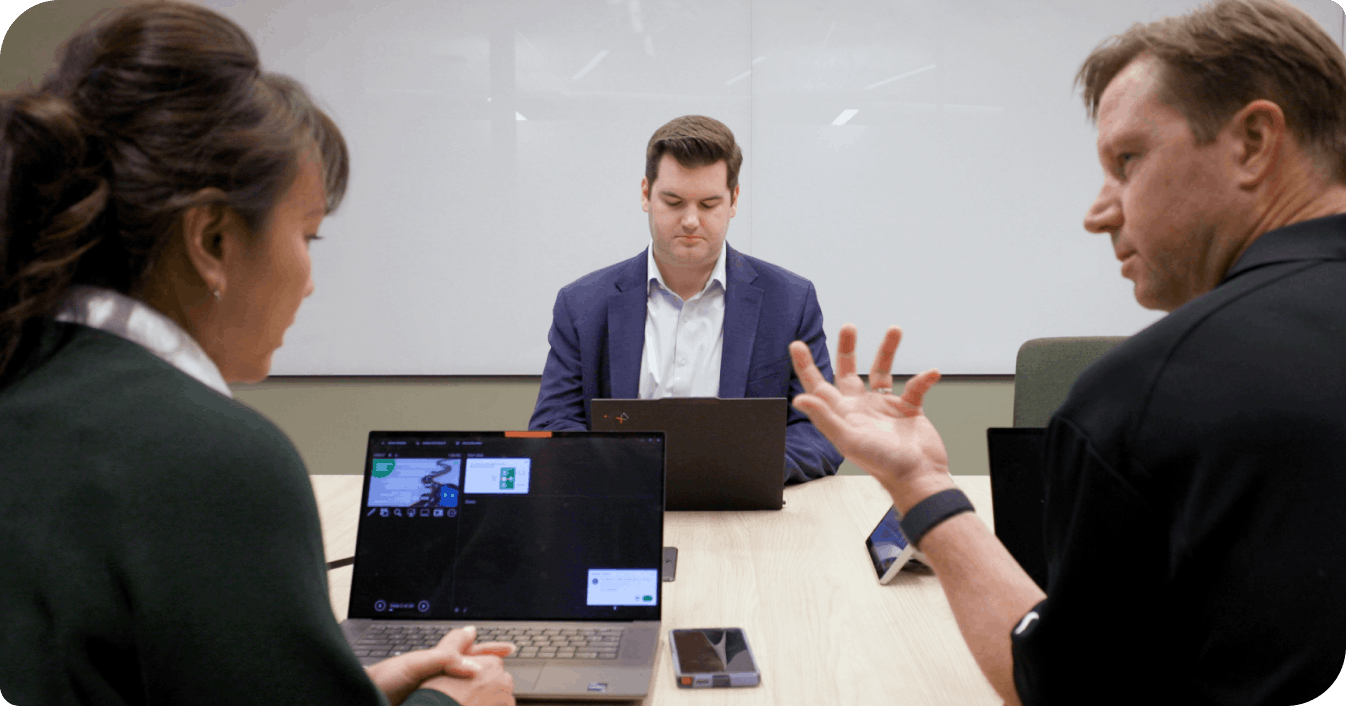 Two colleagues collaborate in a conference room during a hybrid meeting with a video call on a laptop
