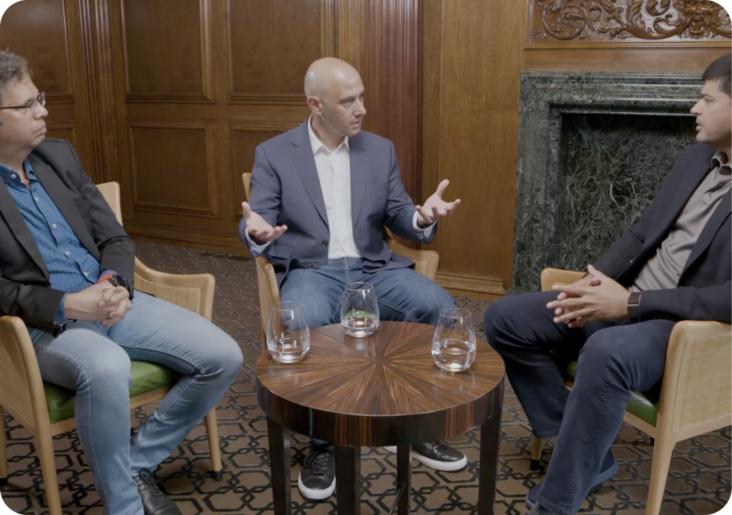 Three men sit in a wood-paneled room, engaged in a discussion around a small table