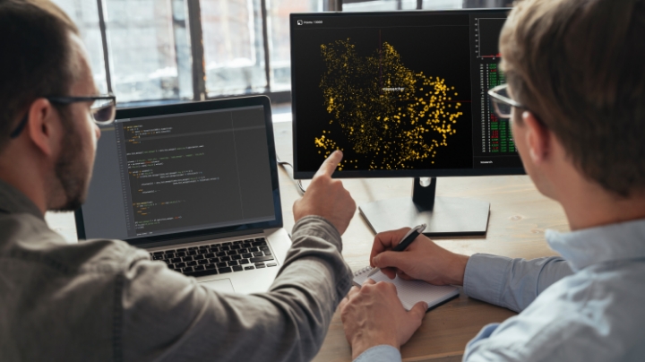 Image of two individuals looking at multiple computer screens