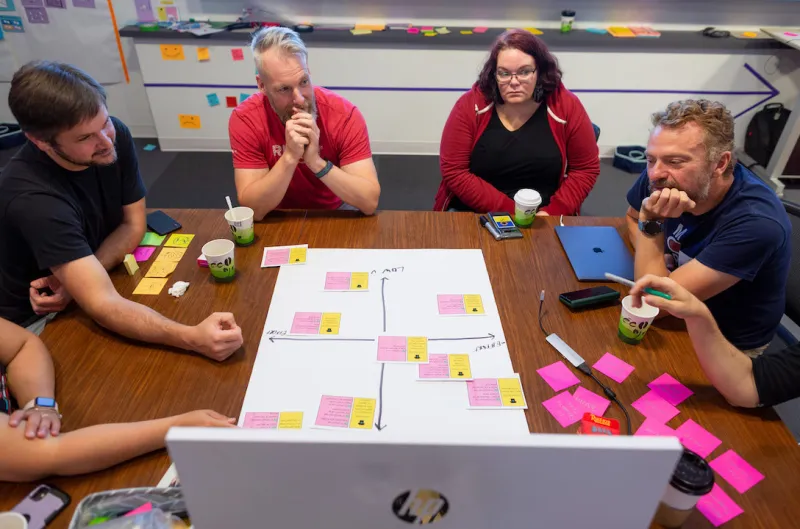 An image of several people seated around a conference table, brainstorming with sticky notes