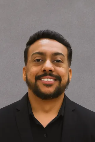 A smiling man with a beard and mustache, wearing a black shirt and blazer