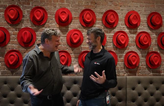 Paul Cormier and Orren Krieger standing in front of a wall of red fedoras.