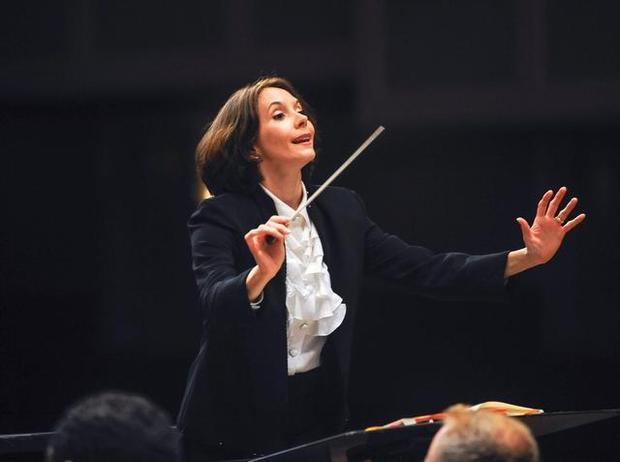 A photograph of a woman in a formal suit conducting an orchestra